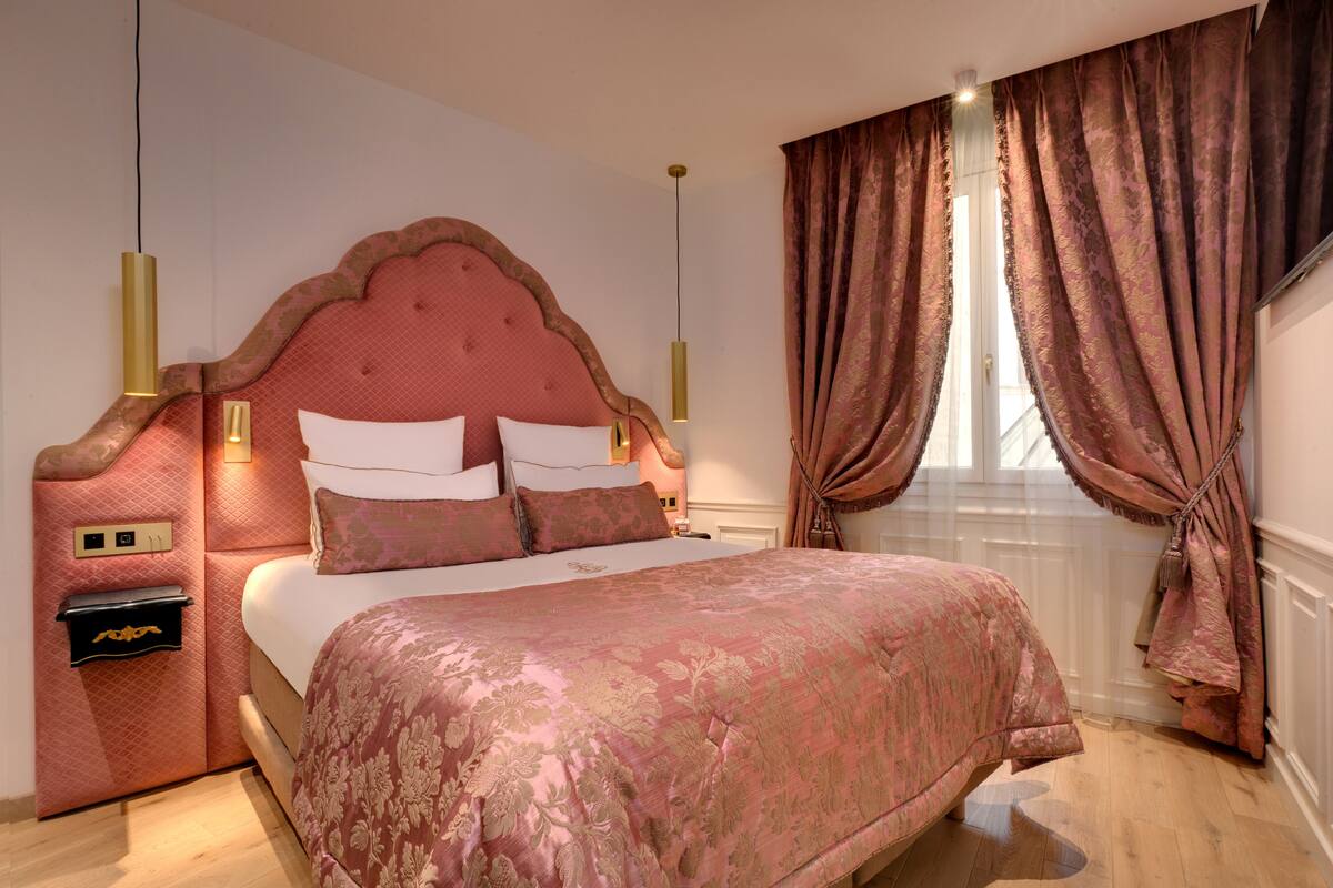 A bedroom with a large bed, a nightstand, a lamp, and a window with curtains.