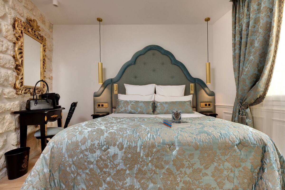 A bedroom with a large bed, a dresser, a mirror, and a window with curtains.