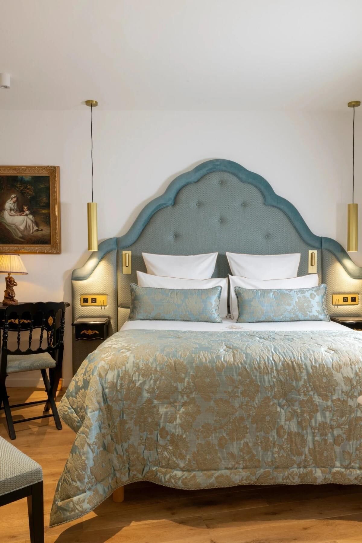 Un lit avec une tête de lit capitonnée, deux tables de chevet avec des lampes, une chaise et un tableau au mur.