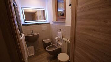 A small bathroom with a wooden floor, a sink, a bidet, and a toilet.