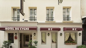 A building with a sign reading "HOTEL DU CYGNE" and "HC" on awnings. There are windows with curtains, a door, and a small balcony. - Hotel du Cygne Paris (Paris)