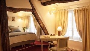 A bedroom with a bed, a desk, and a chair. There is a window with curtains, a lamp, and a wall-mounted light. - Hotel du Cygne Paris (Paris)