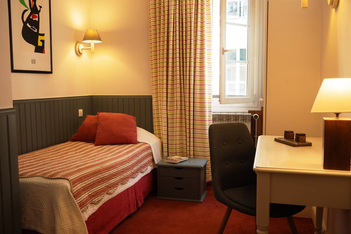 Ein Hotelzimmer mit Bett, Nachttisch, Stuhl und Schreibtisch mit Lampe.