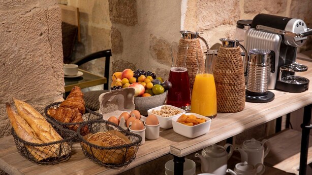 A breakfast buffet with bread, pastries, eggs, and beverages on a wooden table. - Hôtel des Deux-Iles - Notre-Dame (Paris)