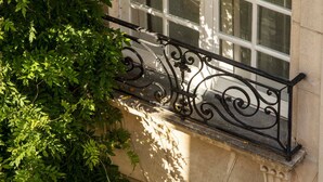 A wrought iron balcony railing with a stone balustrade, overlooking a building with large windows. - Hôtel des Deux-Iles - Notre-Dame (Paris)