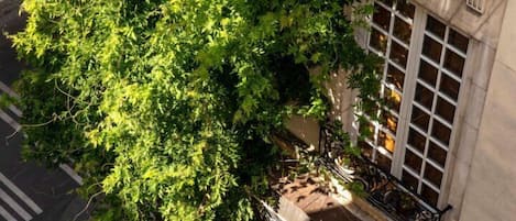 En vy över en gata, tagen från ovan, med ett träd, en trottoar och en byggnad med en balkong.