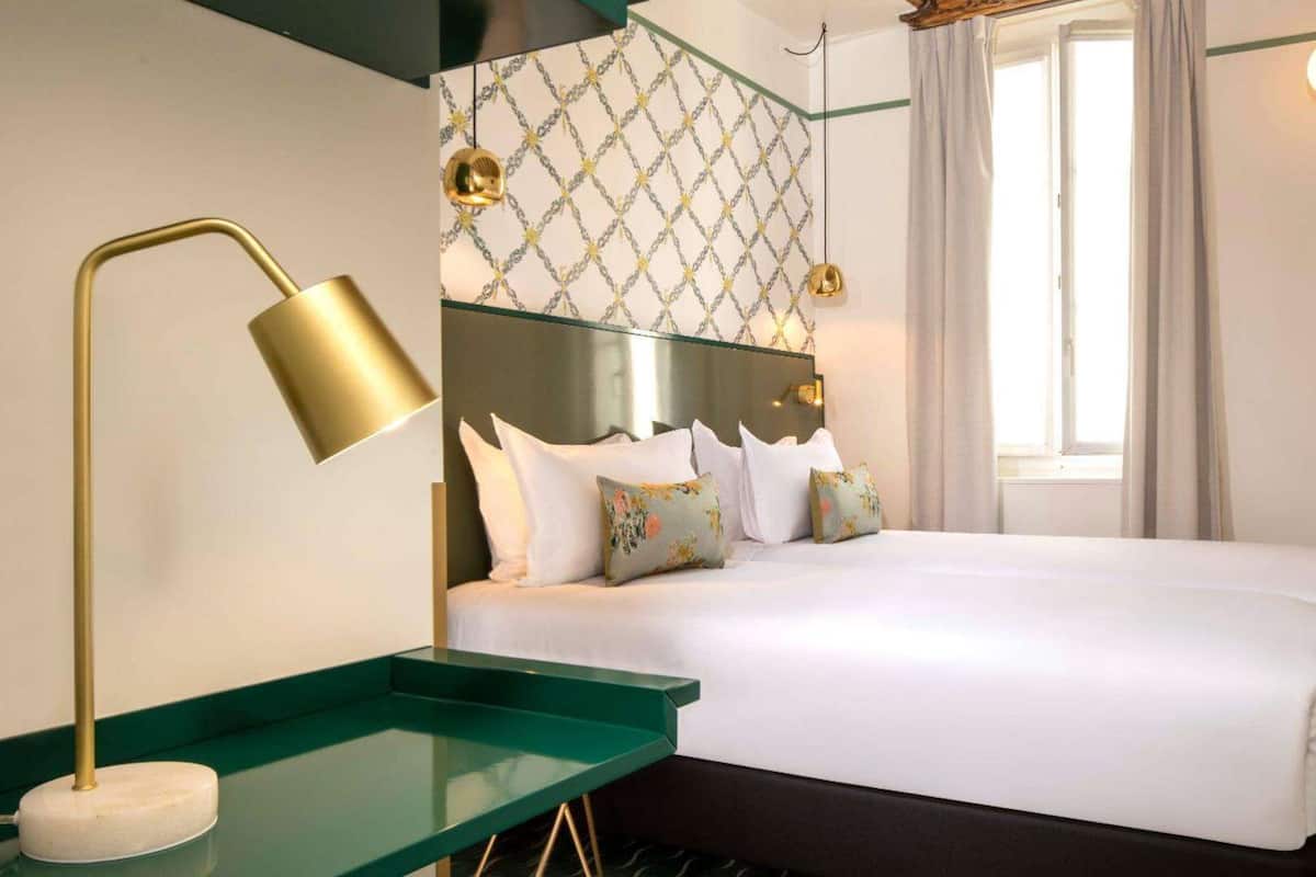 Ein Hotelzimmer mit einem Bett, einem grünen Nachttisch, einer goldenen Lampe und einer Wand mit Muster.