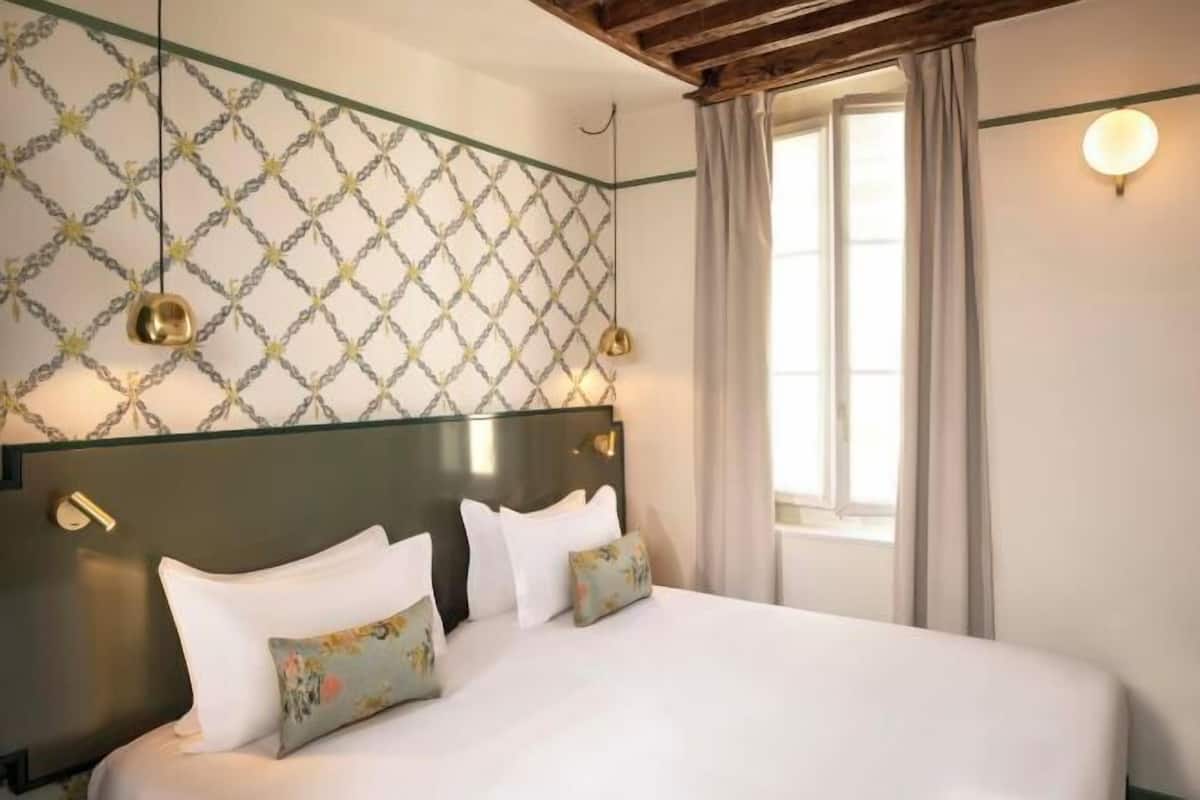 Ein Hotelzimmer mit Bett, Wand mit Muster und Fenster mit Vorhängen.
