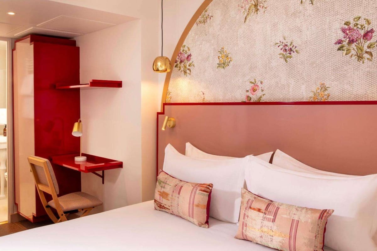 Ein Hotelzimmer mit einem Bett, einem Schreibtisch, einem Stuhl und einem durch eine offene Tür einsehbaren Badezimmer.