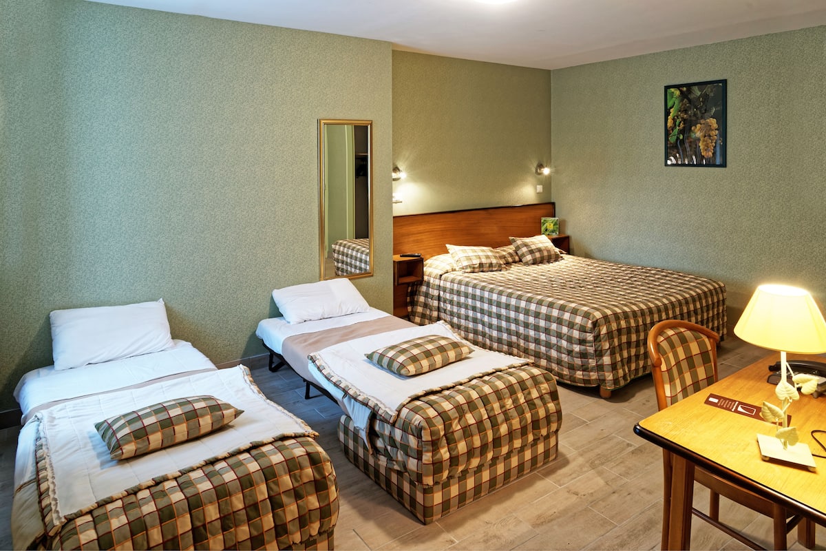 A hotel room with three beds, a wooden headboard, a desk with a lamp, and a mirror.