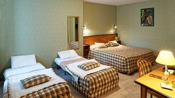 Une chambre d’hôtel avec trois lits, une tête de lit en bois, un bureau avec une lampe et un miroir.