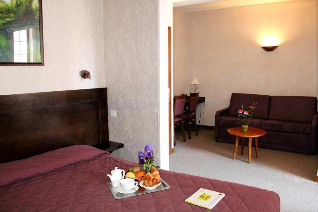 A hotel room with a bed, a dining area with a table and chairs, and a sofa.