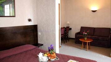 A hotel room with a bed, a dining area with a table and chairs, and a sofa.