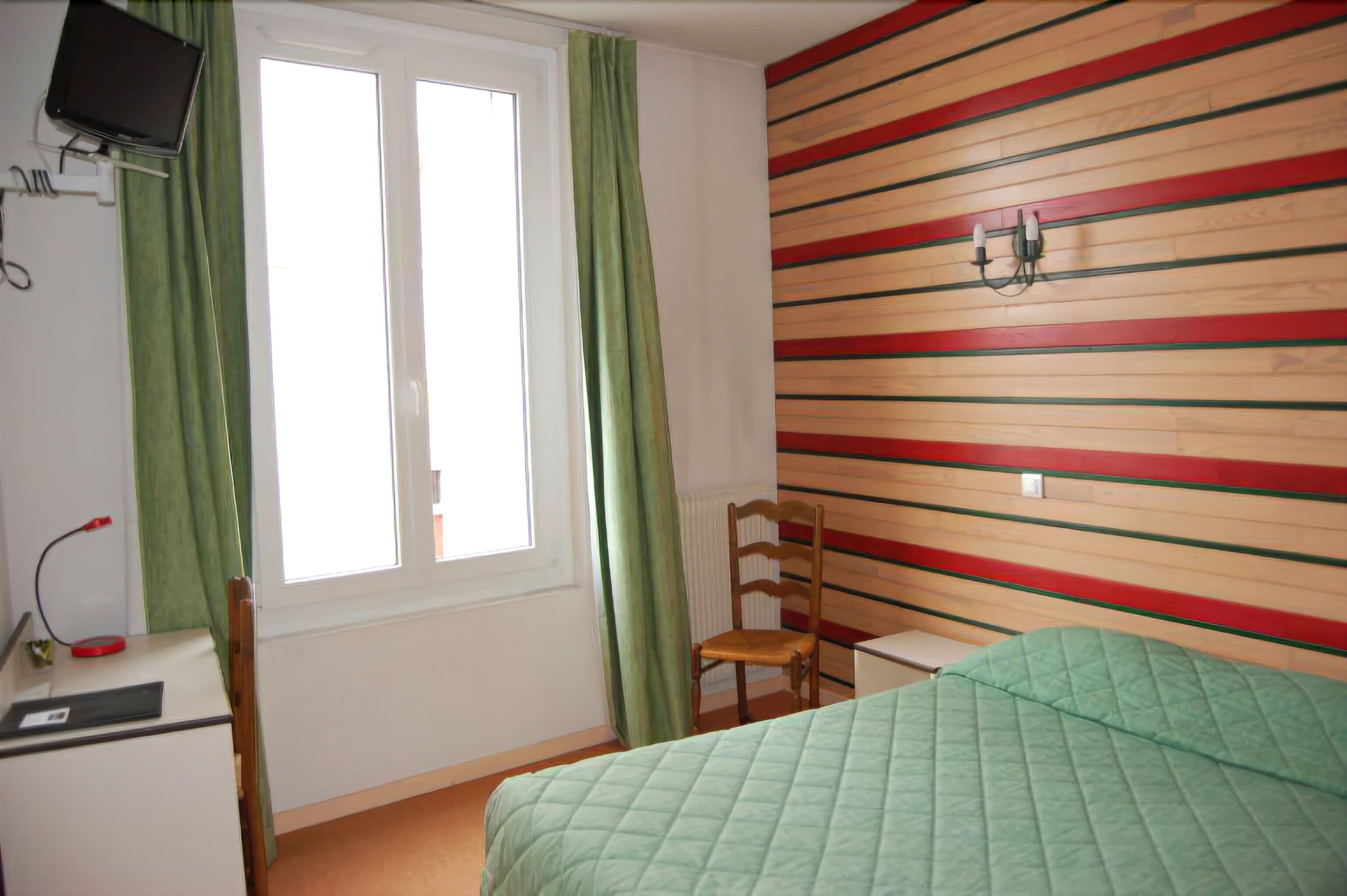 A room with a bed, a desk, a chair, a window with curtains, and a wall with horizontal stripes.