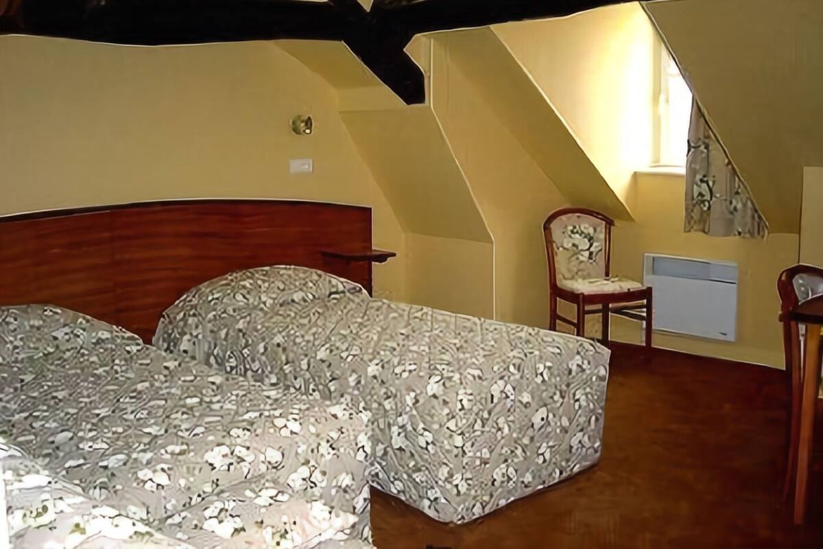 A bedroom with a wooden headboard, a bed with patterned bedding, a chair, and a small desk with a lamp.