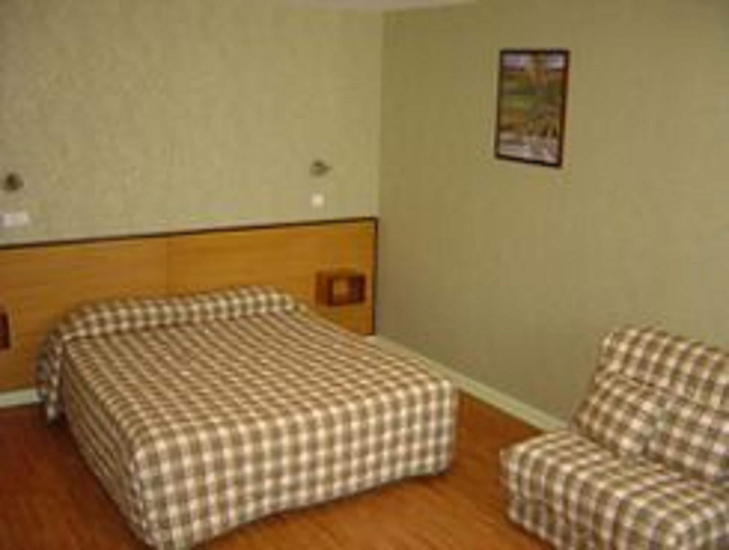 A room with a single bed, a chair, and a wall-mounted picture.