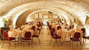 Un comedor interior con paredes de piedra y techos abovedados, con mesas redondas, sillas rojas y manteles blancos.