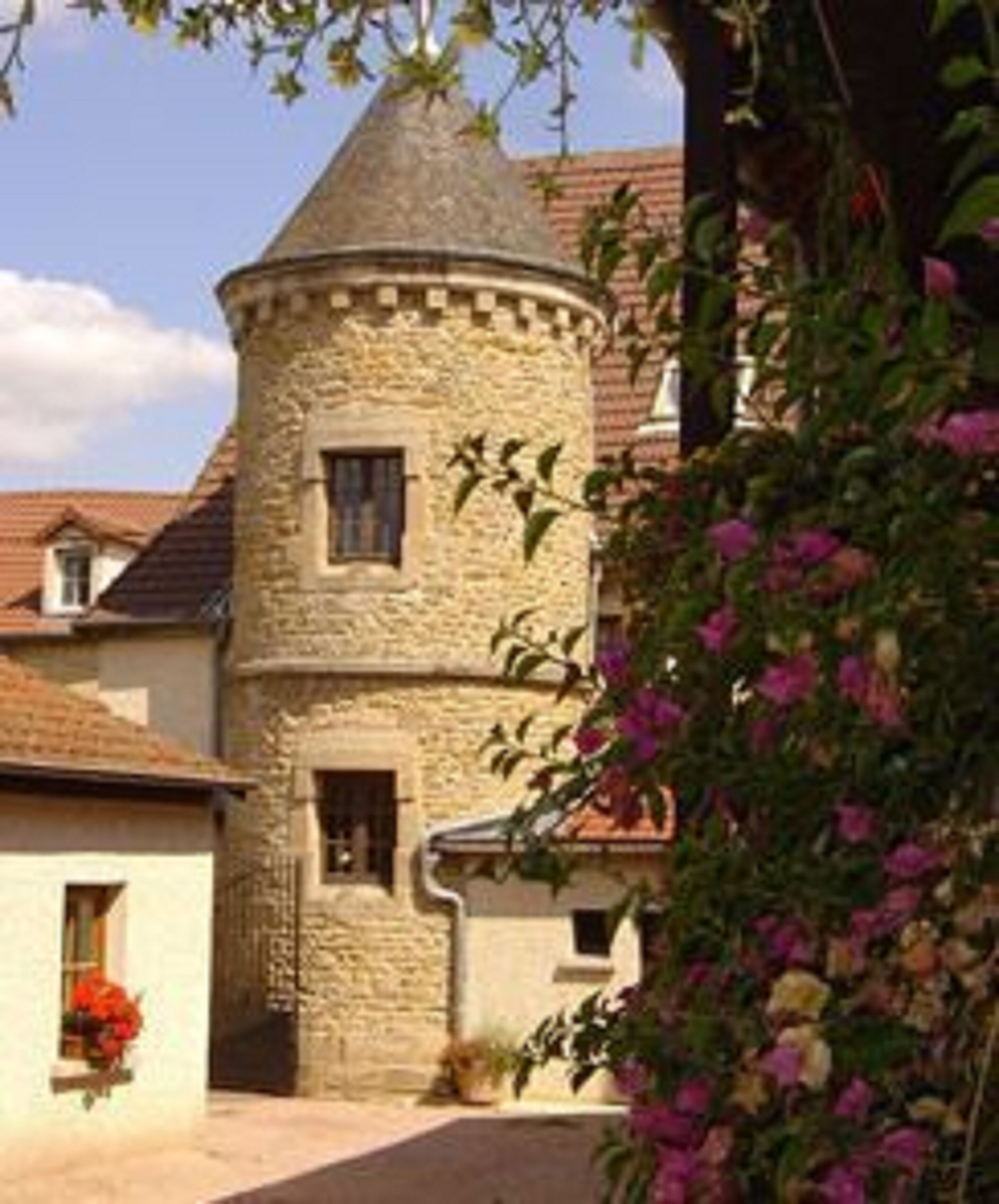 Ein steinerner Turm mit einem kegelförmigen Dach, umgeben von einem Garten mit blühenden Pflanzen.