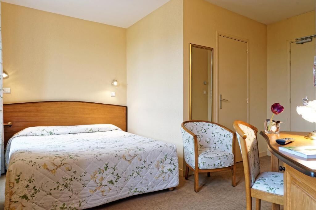 A bedroom with a bed, a chair, a desk, and a mirror.
