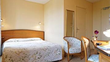 A bedroom with a bed, a chair, a desk, and a mirror.