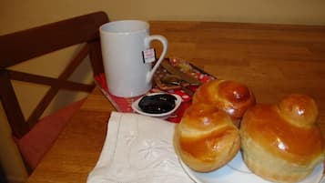 A wooden table with a white mug, a plate of bread rolls, and a small bowl of jam.