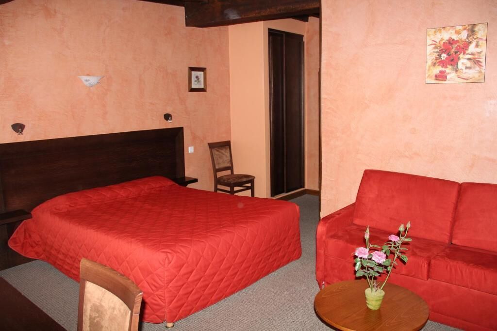 Een kamer met een bed, een rode bank, een kleine tafel met een bloemenvaas en een ingelijst schilderij aan de muur.