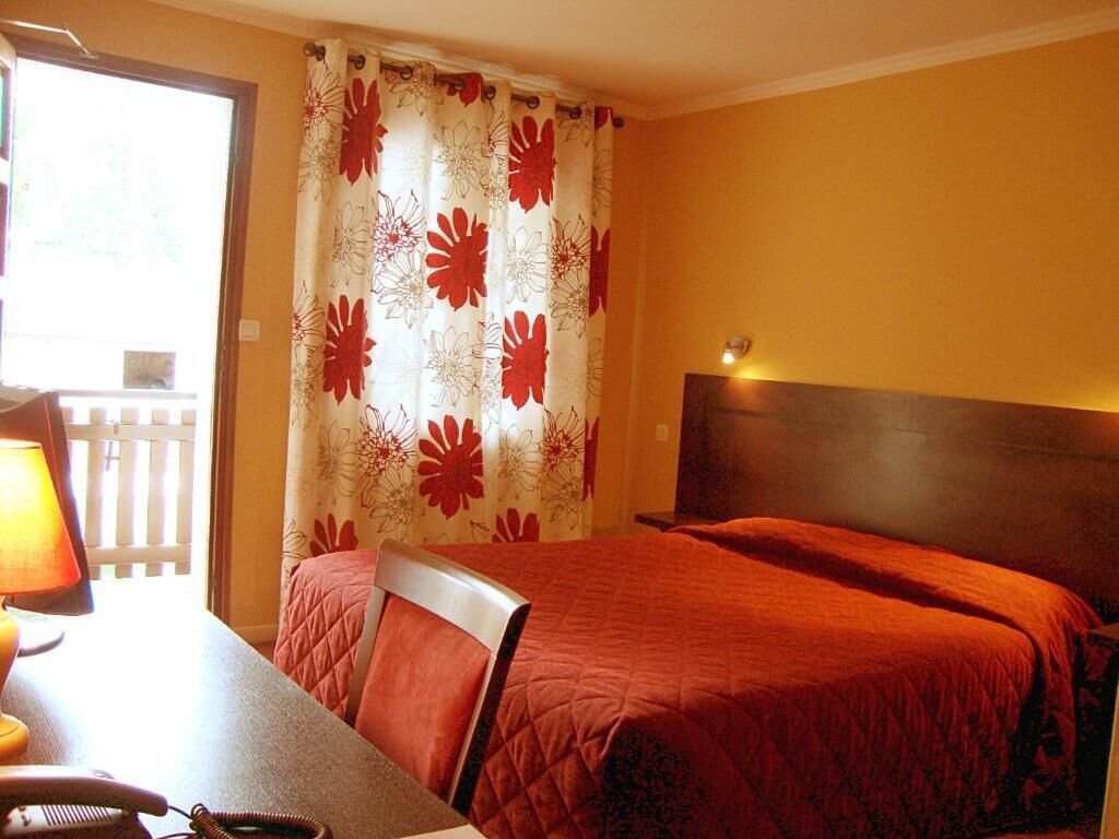 Een hotelkamer met twee bedden, een houten hoofdeinde, een bureau met een lamp en een raam met gordijnen.