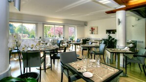 Un comedor espacioso con varias mesas y sillas, amplias ventanas con vista a árboles y un diseño moderno de techo.
