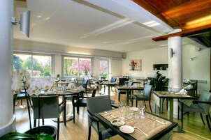Un vaste espace dédié à la salle à manger, avec de nombreuses tables et chaises, de grandes fenêtres offrant une vue sur les arbres et un design moderne au niveau du plafond.