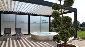 Un espacio exterior moderno con dos sillones de descanso, un jacuzzi y un árbol en maceta.