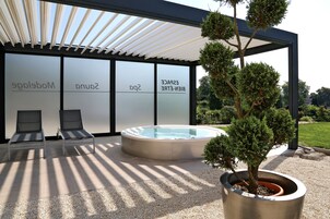 Un espace extérieur moderne comprenant deux fauteuils de jardin, un jacuzzi et un arbre en pot.