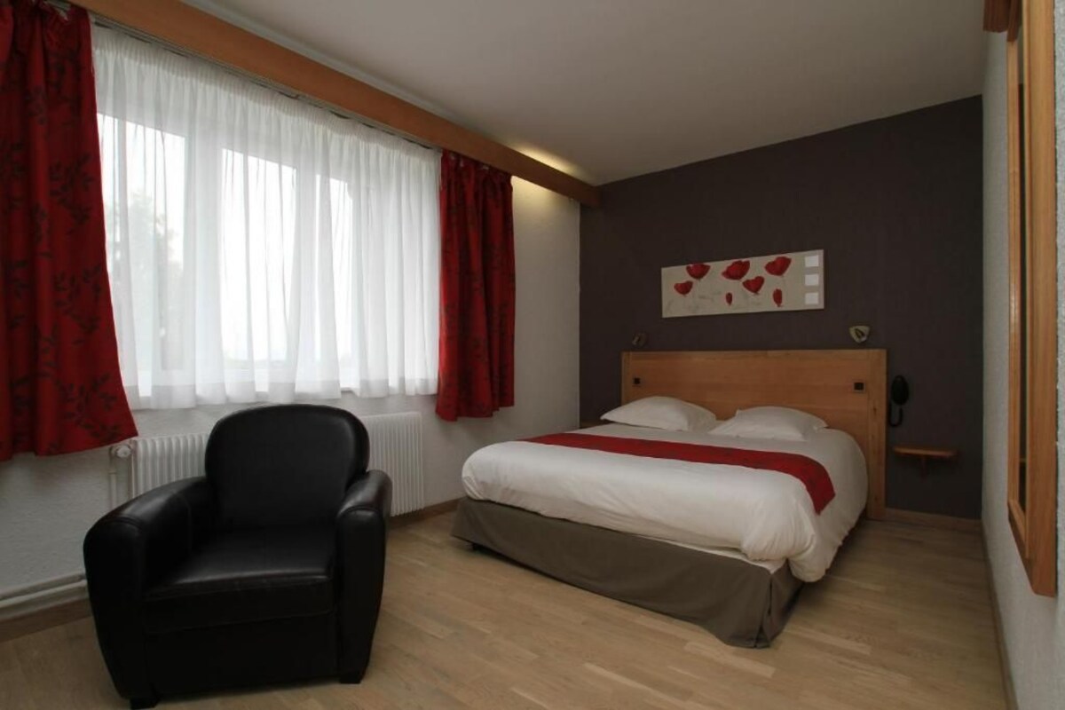 Quarto com cama, cadeira, janela com cortinas e uma obra de arte na parede.