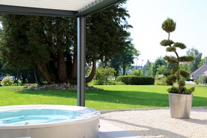 Un bain à remous situé sous une zone abritée, avec une pelouse et des arbres en arrière-plan.