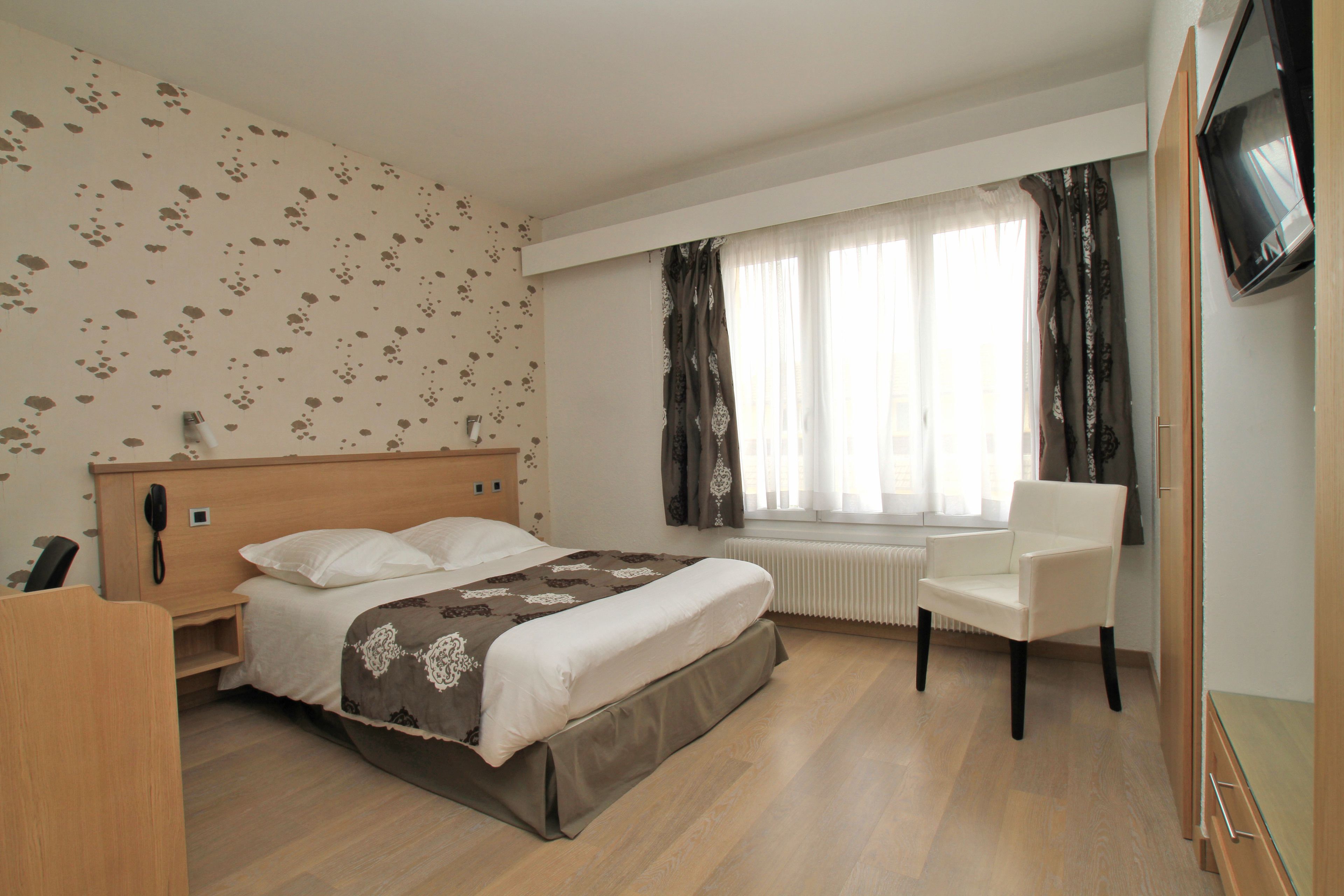 Habitación de hotel con cama, una silla, escritorio, teléfono y televisor.