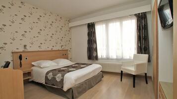 Habitación de hotel con cama, una silla, escritorio, teléfono y televisor.