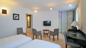 Habitación de hotel con dos camas, un escritorio con lámpara, televisión y una pequeña mesa con sillas.