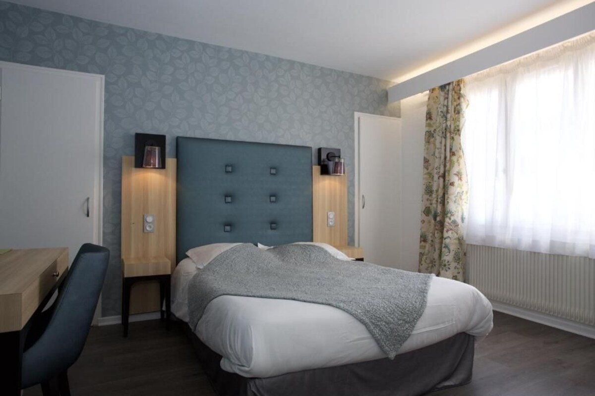 A bedroom with a bed, a desk, and two bedside tables with lamps.