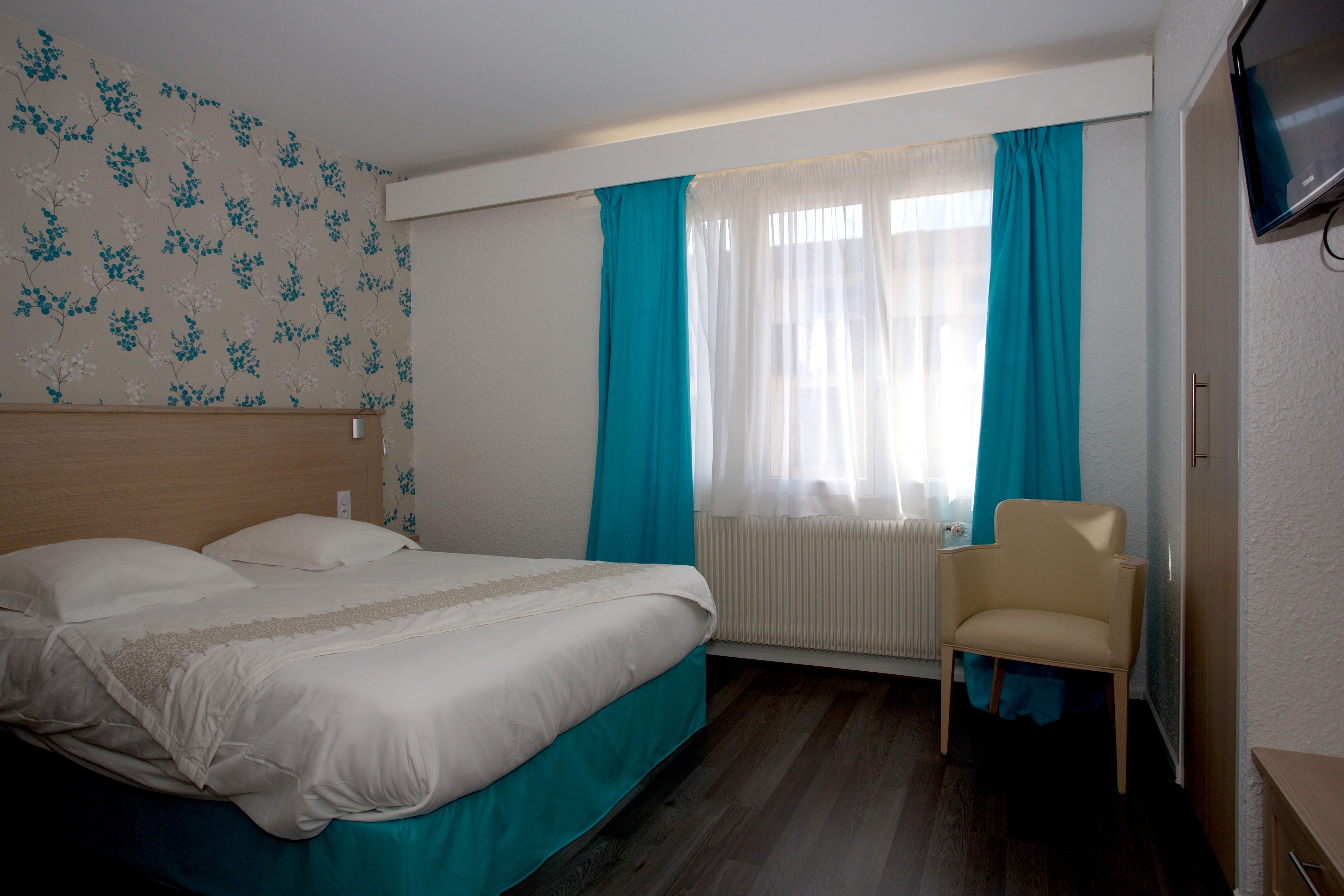 A hotel room with a bed, a chair, a TV, and a window with curtains.