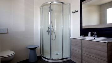 Un bany modern amb dutxa de vidre, vàter i un lavabo amb mirall.