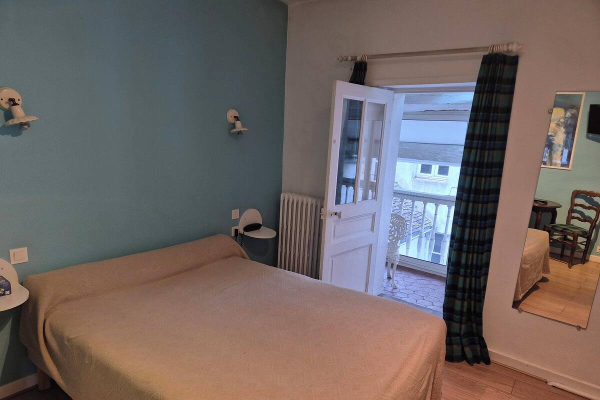 A room with a bed, a radiator, a door leading to a balcony, and a chair.