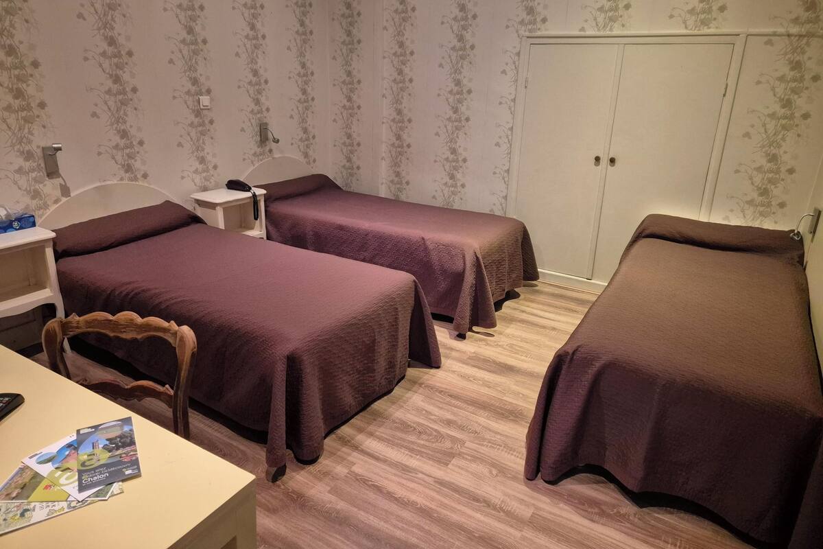 A room with two single beds, a desk, and a chair. There is a wardrobe and a small table with a phone on it.