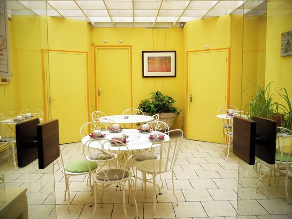 A yellow-walled room with a round table and chairs, a potted plant, and a framed picture on the wall. - Hotel Saint Jean (Chalon-sur-Saone)