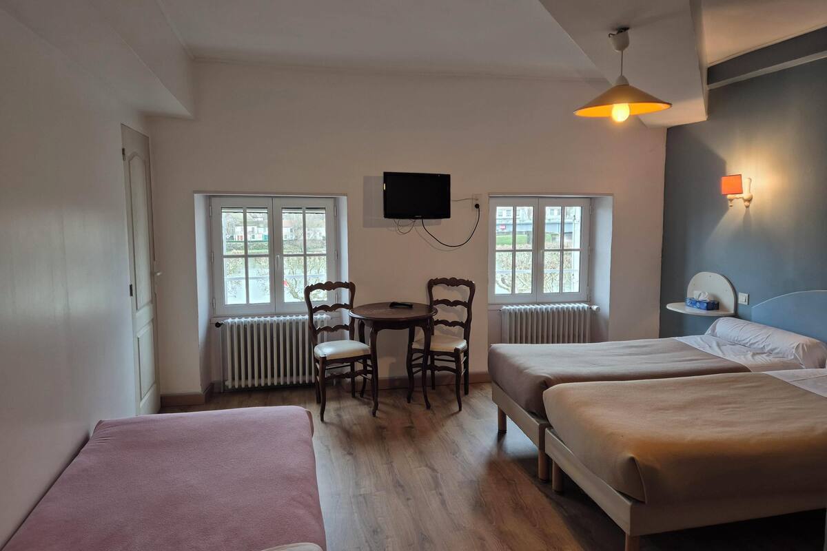 A room with two beds, a table, two chairs, a TV, and two windows.