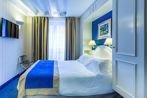 Quarto de hotel com uma cama, uma televisão presa na parede, um abajur e um quadro na parede.