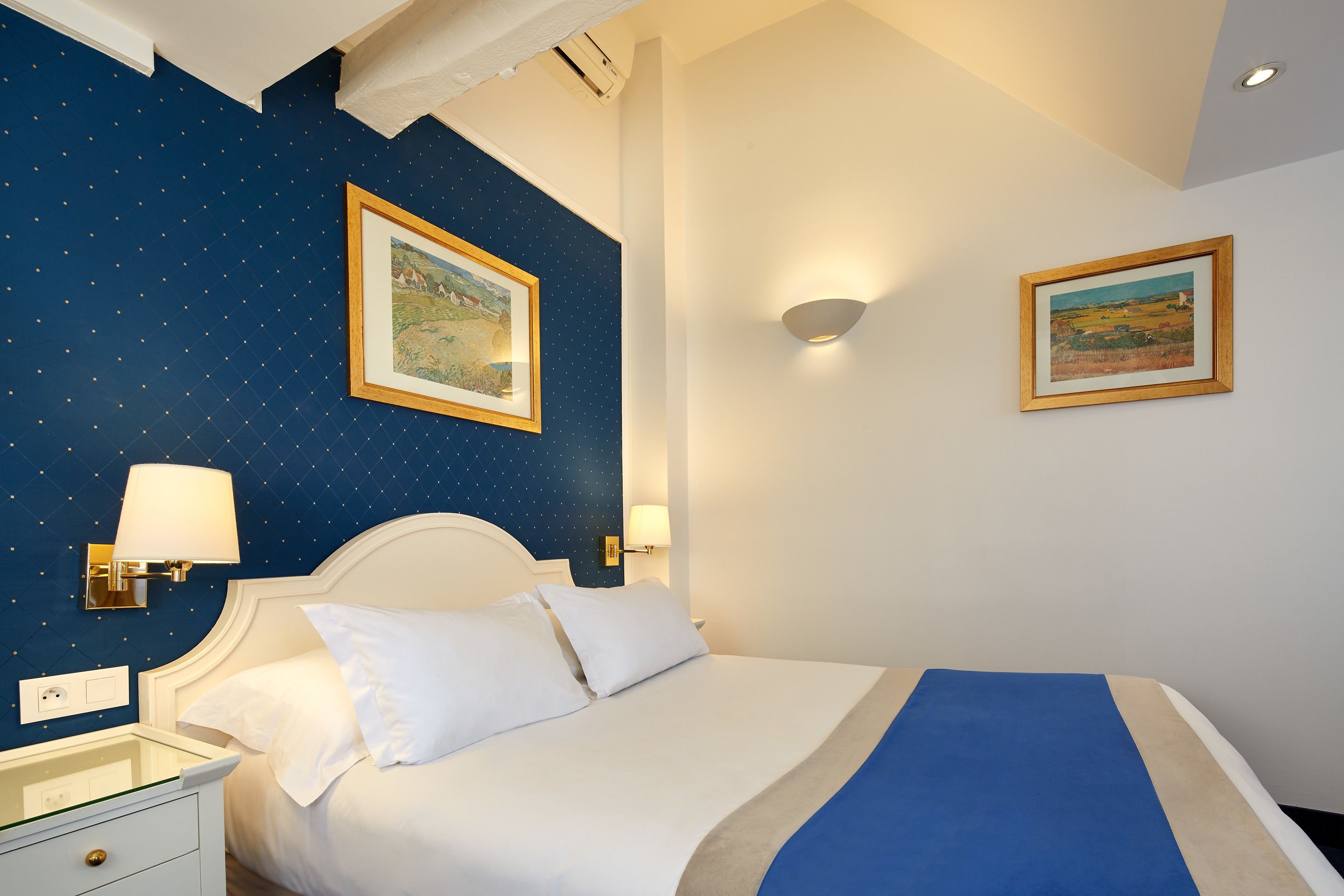 A hotel room with a bed, nightstand, and two wall-mounted lamps.