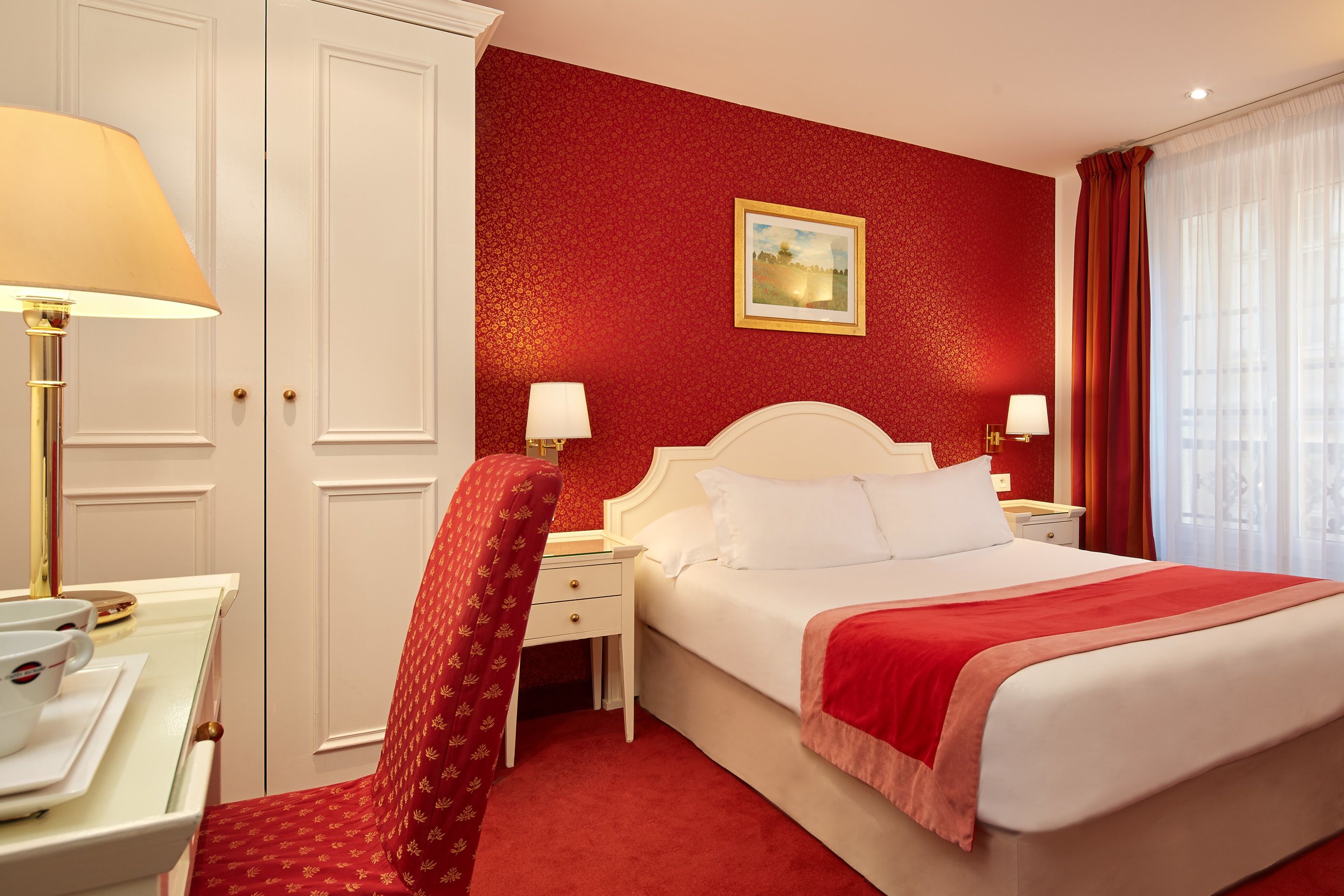 A hotel room with a large bed, a desk with a lamp, a chair, and a nightstand.