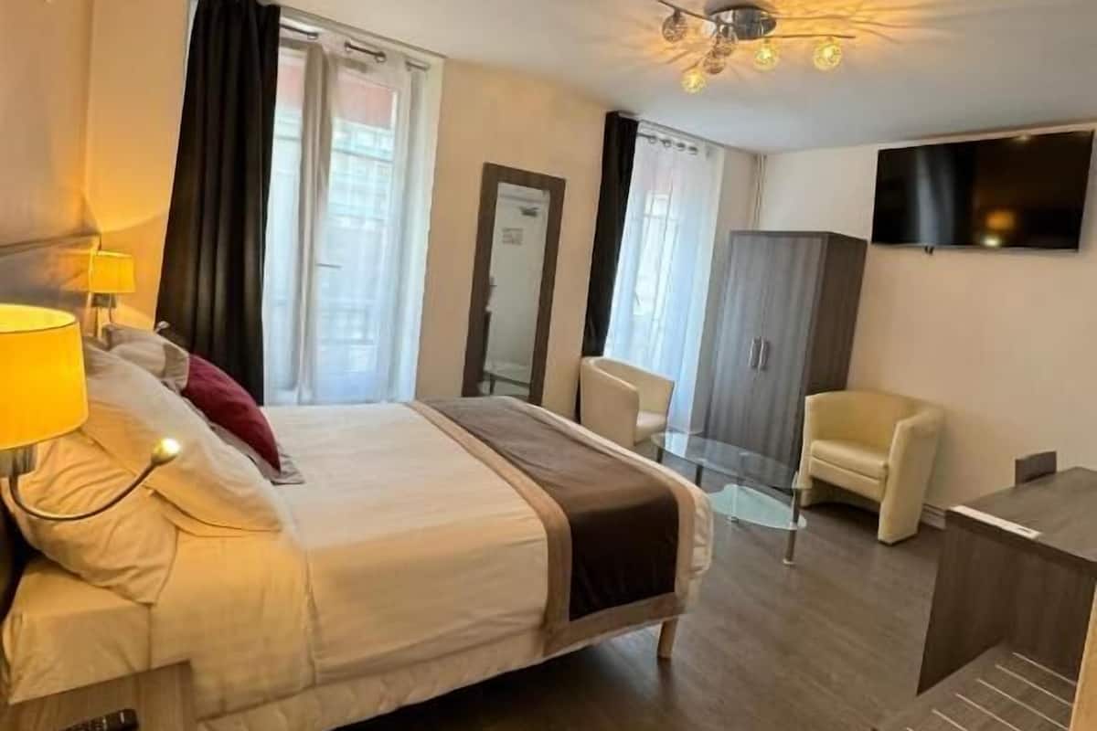 A hotel room with a bed, bedside lamp, chair, desk, TV, and a mirror.