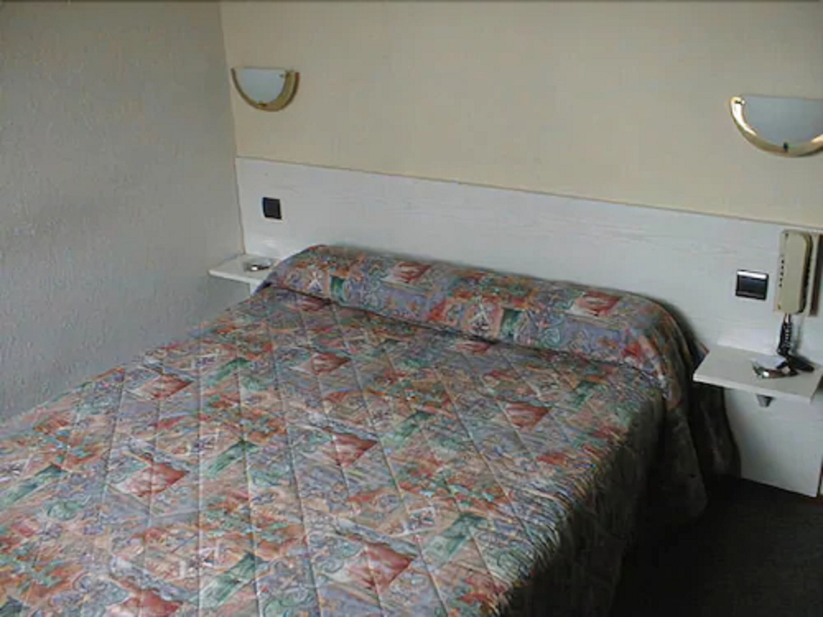 A standard hotel room with a single bed, a nightstand, a bedside table, and a mirror.