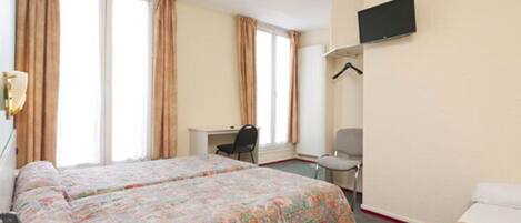 A hotel room with two beds, a desk, a chair, a TV, and large windows with curtains.