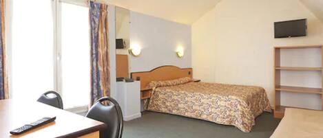 A hotel room with a bed, a desk, a chair, a TV, and a bookshelf.